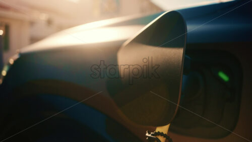 Video - Close up of an electric vehicle charging connector plugged into a car, with warm sunset light and lens flare