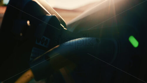 Video - Close up of an electric vehicle charging connector plugged into a car, with warm sunset light and lens flare