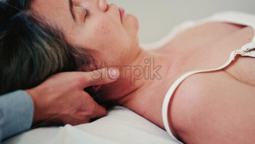 Video - Side profile of a woman resting on a treatment table while a therapist supports her neck and head during a calm manual therapy session