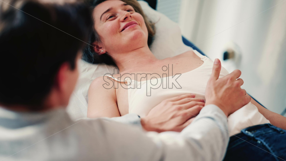 Video - Therapist examines a woman lying on a medical bed, placing hands on the abdomen as part of an assessment or treatment