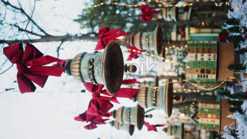 Video - Decorative hanging bells with red bows and warm string lights outdoors. Vertical
