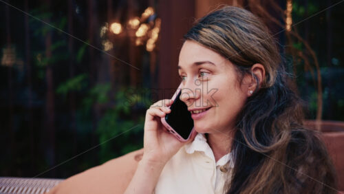Video - Woman sitting outdoors while talking on a smartphone, looking thoughtful