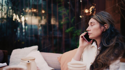 Video - Woman sitting outdoors while talking on a smartphone, looking thoughtful