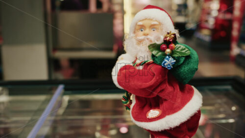 Video - Santa Claus figurine holding a green gift bag decorated with small presents, moving