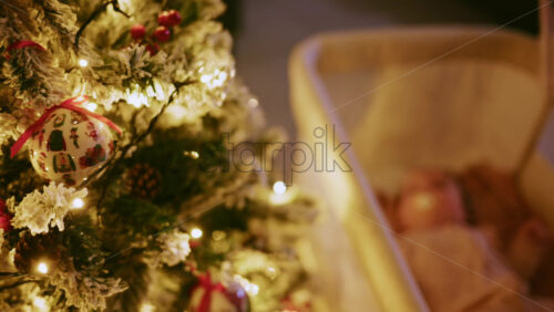 Video - Warm and intimate Christmas scene featuring a baby lying peacefully in a cradle beside a softly illuminated Christmas tree