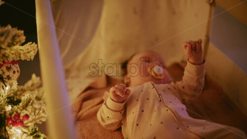 Video - Close up of a baby with a pacifier illuminated by warm Christmas lights, creating a joyful and heartwarming holiday mood