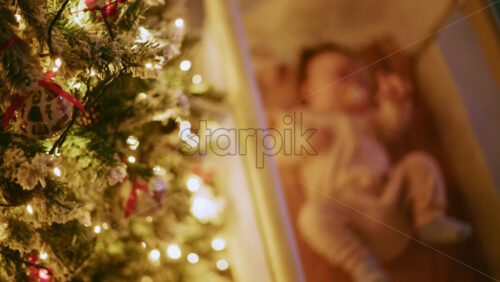 Video - Warm and intimate Christmas scene featuring a baby lying peacefully in a cradle beside a softly illuminated Christmas tree