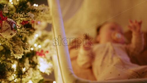 Video - Warm and intimate Christmas scene featuring a baby lying peacefully in a cradle beside a softly illuminated Christmas tree