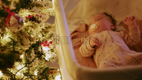Video - Warm and intimate Christmas scene featuring a baby lying peacefully in a cradle beside a softly illuminated Christmas tree