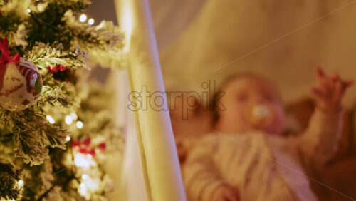 Video - Warm and intimate Christmas scene featuring a baby lying peacefully in a cradle beside a softly illuminated Christmas tree