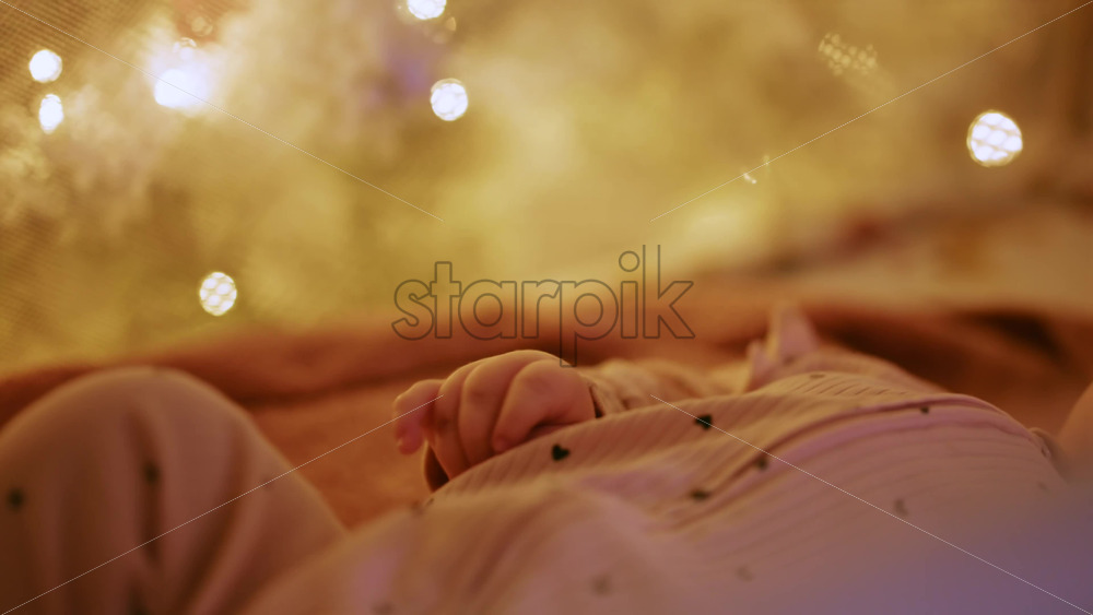 Video - Close up of a baby's hand with warm Christmas lights in the background