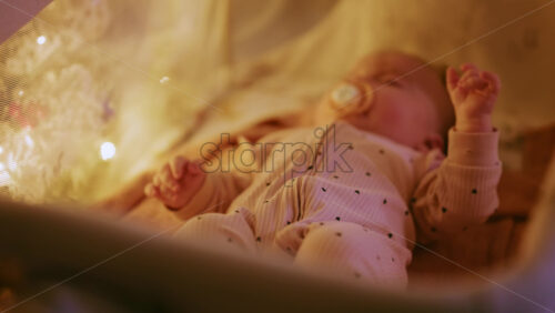 Video - Close up of a baby with a pacifier illuminated by warm Christmas lights, creating a joyful and heartwarming holiday mood