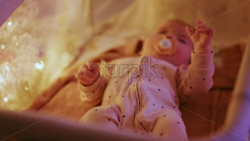 Video - Close up of a baby with a pacifier illuminated by warm Christmas lights, creating a joyful and heartwarming holiday mood