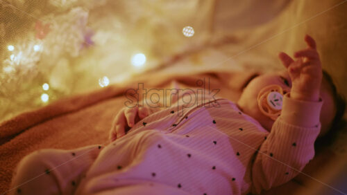 Video - Close up of a baby with a pacifier illuminated by warm Christmas lights, creating a joyful and heartwarming holiday mood