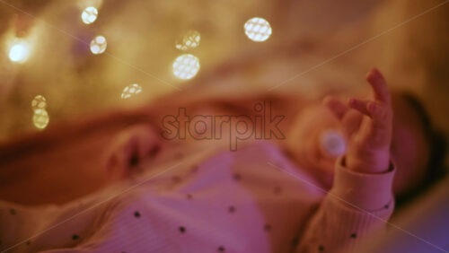 Video - Close up of a baby with a pacifier illuminated by warm Christmas lights, creating a joyful and heartwarming holiday mood