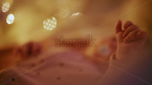 Video - Close up of a baby's hand with warm Christmas lights in the background