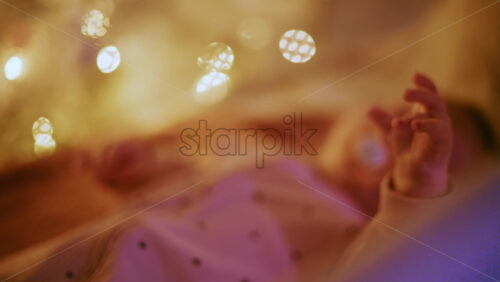Video - Close up of a baby's hand with warm Christmas lights in the background