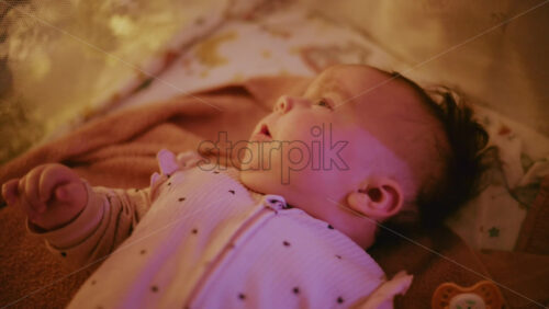 Video - Close up of a baby illuminated by warm Christmas lights, creating a joyful and heartwarming holiday mood