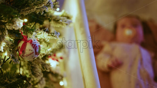 Video - Warm and intimate Christmas scene featuring a baby lying peacefully in a cradle beside a softly illuminated Christmas tree