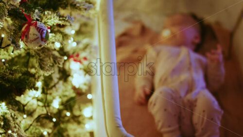 Video - Warm and intimate Christmas scene featuring a baby lying peacefully in a cradle beside a softly illuminated Christmas tree