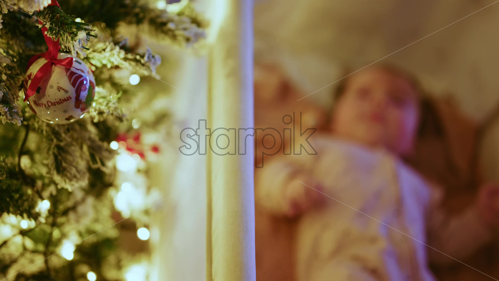 Video - Warm and intimate Christmas scene featuring a baby lying peacefully in a cradle beside a softly illuminated Christmas tree