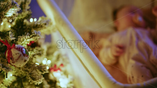 Video - Warm and intimate Christmas scene featuring a baby lying peacefully in a cradle beside a softly illuminated Christmas tree