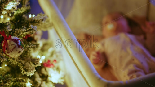 Video - Warm and intimate Christmas scene featuring a baby lying peacefully in a cradle beside a softly illuminated Christmas tree