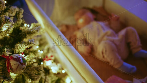 Video - Warm and intimate Christmas scene featuring a baby lying peacefully in a cradle beside a softly illuminated Christmas tree
