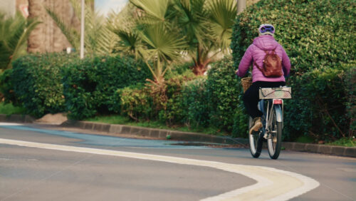 Video - Golfe Juan, France - December 15, 2025: Woman cycling along a quiet urban road surrounded by greenery