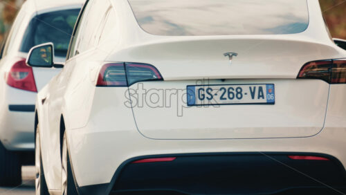 Video - Golfe Juan, France - December 15, 2025: Rear view of a modern, white Tesla car waiting in traffic on a city road