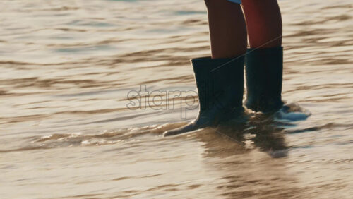 Video - Close up of a child's legs wearing waterproof boots while standing in shallow sea water