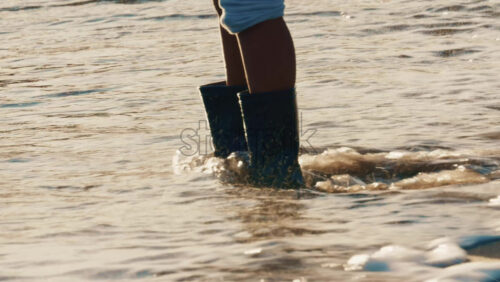 Video - Close up of a child's legs wearing waterproof boots while standing in shallow sea water