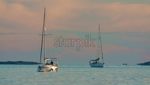 Video - Wide shot of sailboats anchored on calm open water with distant shoreline in the background