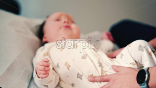 Video - Adult hand gently rests on a baby's torso while the infant lies on a padded surface