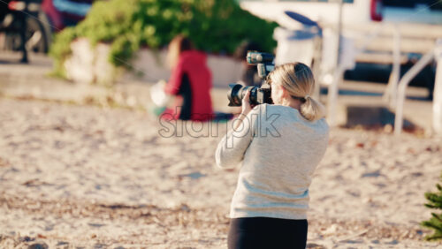 Video - Rear view of a blonde woman photographer holding a camera and taking photos outdoors in natural light