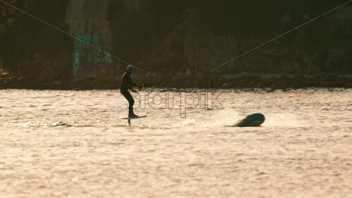 Video - Silhouette of a person riding an electric surfboard on calm sea water during golden hour