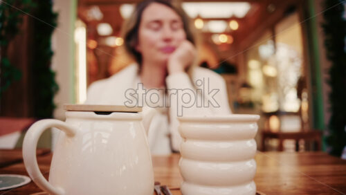 Video - Woman holding a reusable collapsible cup while sitting at a wooden table in a cozy cafe