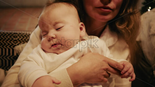 Video - Close-up of a mother gently holding a sleeping baby in a warm indoor setting