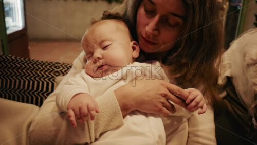 Video - Close-up of a mother gently holding a sleeping baby in a warm indoor setting