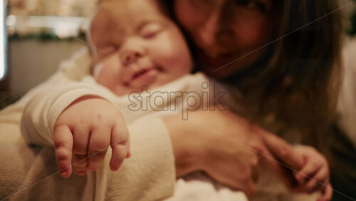 Video - Close-up of a mother gently holding a sleeping baby in a warm indoor setting