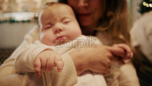 Video - Close-up of a mother gently holding a sleeping baby in a warm indoor setting