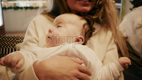 Video - Close-up of a mother gently holding a sleeping baby in a warm indoor setting