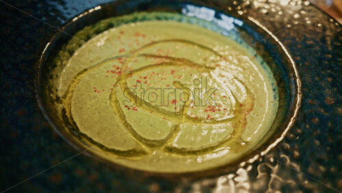 Video - Top view of a creamy green soup garnished with oil and spices, served in a ceramic bowl on a wooden table