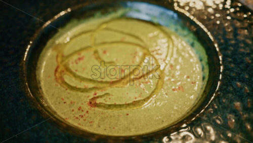 Video - Top view of a creamy green soup garnished with oil and spices, served in a ceramic bowl on a wooden table