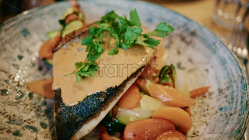 Video - Close up of a plated fish fillet served with vegetables and creamy sauce in a restaurant setting