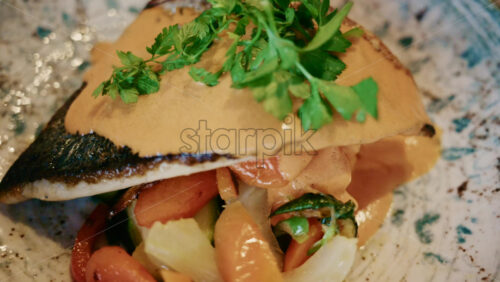 Video - Close up of a plated fish fillet served with vegetables and creamy sauce in a restaurant setting