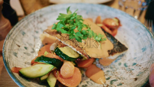 Video - Close up of a plated fish fillet served with vegetables and creamy sauce in a restaurant setting