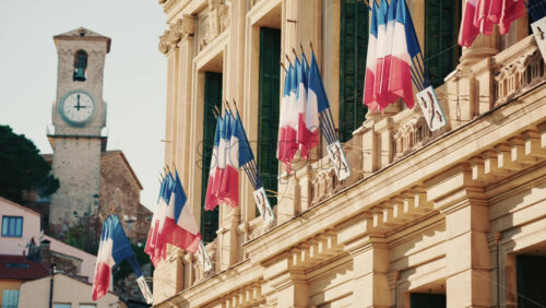Video - Wide shot of a historic building decorated with French tricolor flags under clear daylight