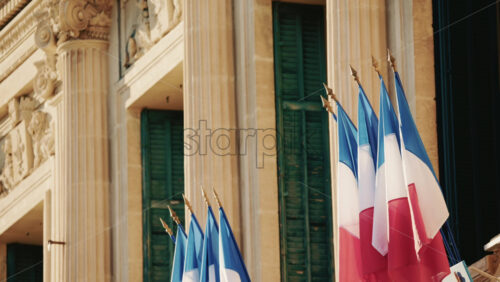 Video - Wide shot of a historic building decorated with French tricolor flags under clear daylight