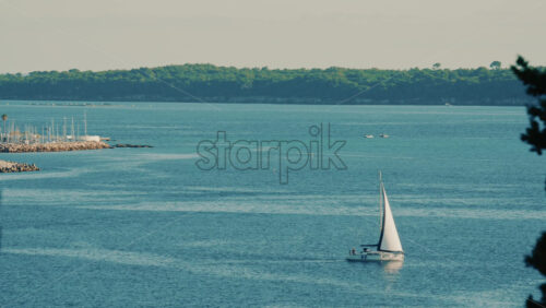 Video - Single sailboat moving across calm blue water under clear sky